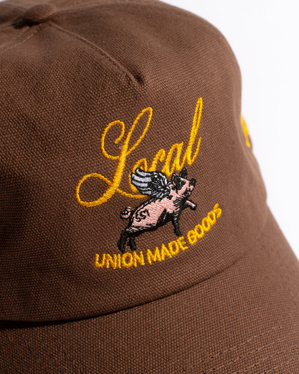 Brown cap with yellow embroidered text and a pig graphic on a white background