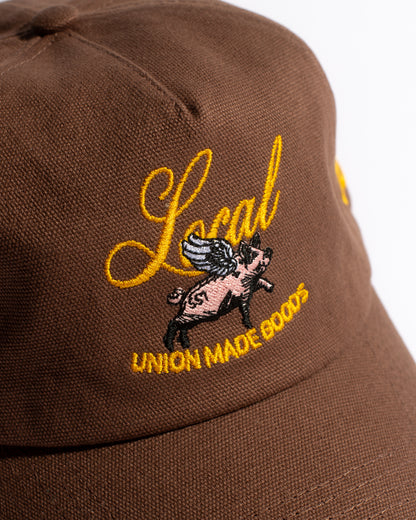 Brown cap with yellow embroidered text and a pig graphic on a white background